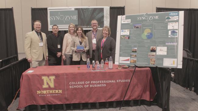 Professors, student and business entrepreneurship representatives standing at competition table