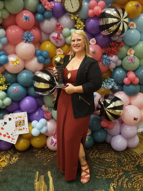 Chelsea Speck holds the ABBY Award give to Sodexo/NSU catering in front of a balloon wall