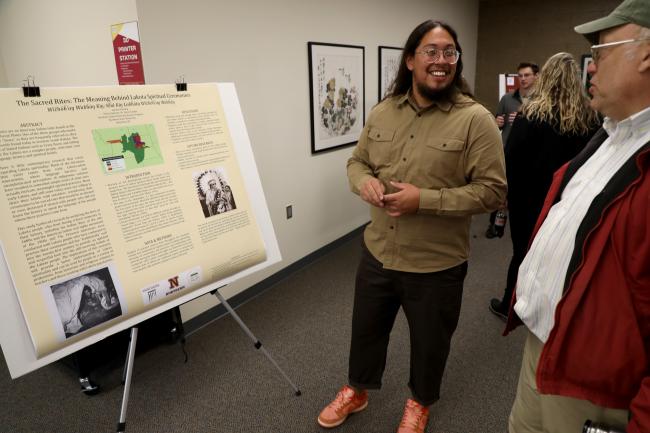 Jaeden Shaving, middle, presents his Honors research poster to Dr. David Grettler, far right, at Northern State University. 