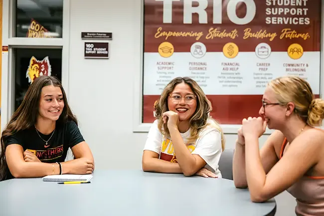 Three students sitting at a round table smiling.